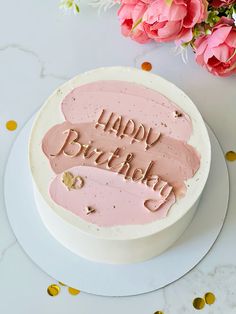 a birthday cake with the words happy birthday written on it and some pink flowers in the background