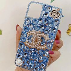 a person holding up a phone case with blue jewels and diamonds on it in front of a white background