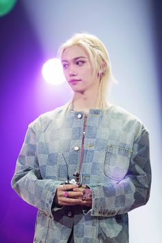 a man with blonde hair standing in front of a purple and blue background wearing a jacket