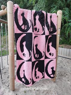 a pink and black crocheted blanket hanging from a wooden frame on the ground