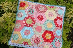 a patchwork quilt is hanging on a tree branch in front of some bushes and green leaves