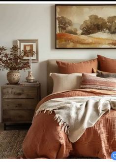 a bed with an orange comforter and pillows in front of a painting on the wall