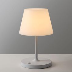 a white table lamp sitting on top of a desk next to a gray and white wall