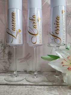 three wine glasses with gold lettering on them sitting next to a flower and wallpaper