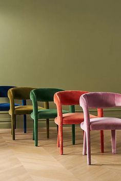 six chairs in different colors are lined up against a wall and floor, with one chair facing the other