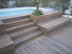 a wooden deck next to a swimming pool with steps leading up to it and potted plants on the side