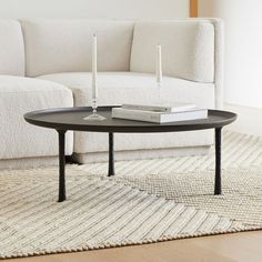 a coffee table with two candles on it in front of a white couch and rug