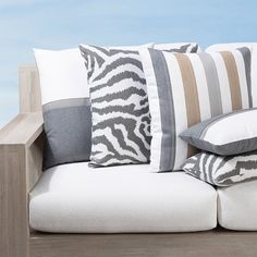 a couch with several pillows on it sitting next to a wooden table and blue sky in the background