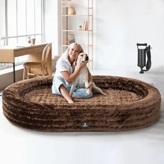 a woman sitting on the floor with her dog in a large round bed that is made out of plush material