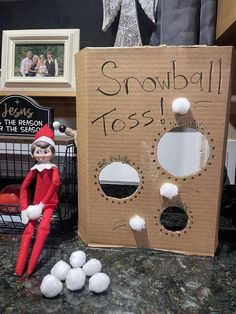 an elf is sitting in front of a cardboard box that says snowball toss