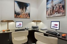 two computer monitors sitting on top of a desk next to each other in front of paintings