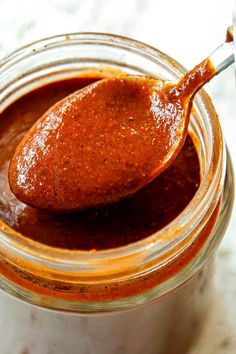 a spoon full of sauce sitting on top of a glass jar filled with chili paste