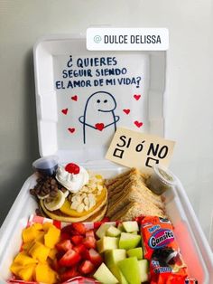 a plastic container filled with lots of fruit and veggies next to a sign