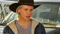 a woman wearing a black cowboy hat standing in front of a car