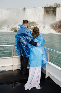 a man and woman wrapped in plastic standing on the deck of a boat near a waterfall