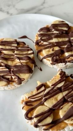 three desserts on a white plate with chocolate drizzled over them and bananas