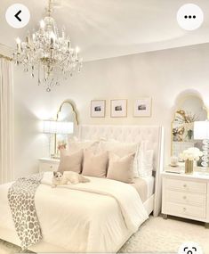 a white bedroom with a chandelier hanging from the ceiling and pillows on the bed