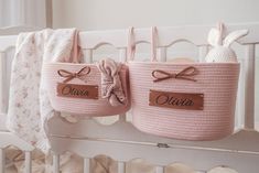 two pink baskets hanging from the side of a crib with name tags on them