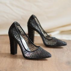 a pair of black high heeled shoes sitting on top of a wooden floor next to a white sheet