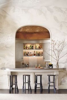 a bar with stools and bottles on the shelves in a room that has floral wallpaper