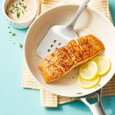 a fish fillet in a skillet with lemon wedges