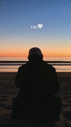 the silhouette of a person sitting on top of a beach next to the ocean at sunset