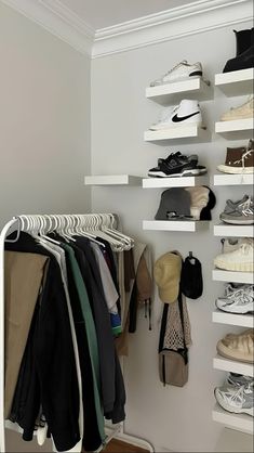 a closet filled with lots of different types of shoes and clothing hanging on white shelves