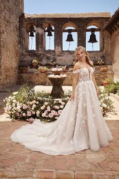 a woman standing in front of a fountain wearing a wedding dress with flowers on it