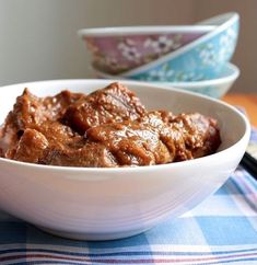 a bowl filled with meat sitting on top of a blue and white checkered table cloth