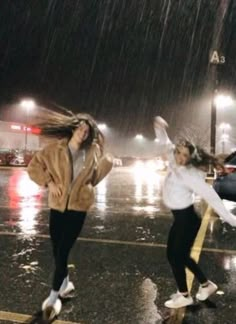 two girls jumping in the rain with their hands up and one girl holding an umbrella