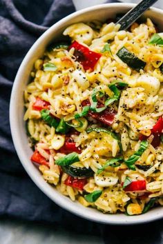 a white bowl filled with pasta and vegetables on top of a table next to a black napkin