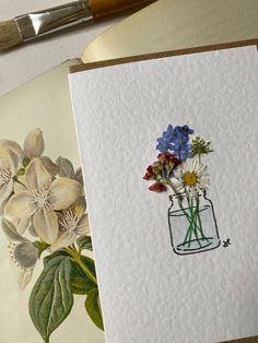 some flowers are in a vase on top of a piece of paper next to a paintbrush