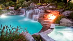 an outdoor swimming pool with waterfall and fire pit in the middle, surrounded by greenery