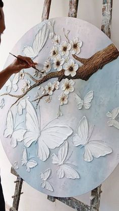 a woman is painting flowers and butterflies on a round wall hanging in front of an easel