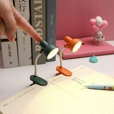 a hand is pointing at two lights on a desk next to books and a pen