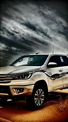 a silver truck parked in the desert under a cloudy sky