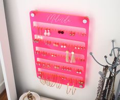 a pink wall mounted jewelry rack on the side of a white wall next to a pair of earrings