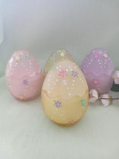 three decorated eggs sitting next to each other on a white tablecloth with flowers in the background