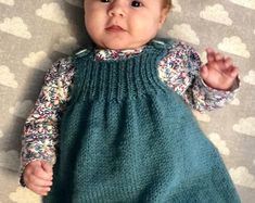 a baby wearing a green dress laying on top of a bed next to a blanket