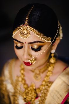 a woman wearing gold jewelry and makeup looks down at her face as she stands in front of the camera