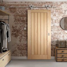 a bedroom with brick wall and wooden closet doors in the corner, along with clothes on hangers