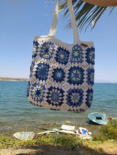 a crocheted tote bag hanging from a palm tree next to the ocean