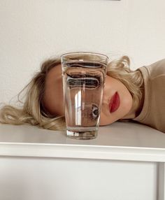 a woman laying on a table with a glass of water in front of her face