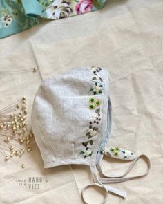 a white hat with flowers on it sitting on top of a table next to some thread