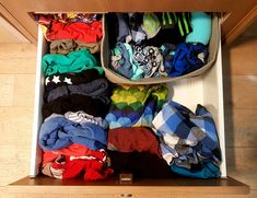 an open drawer filled with clothes on top of a wooden floor