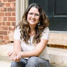 a woman sitting on the steps with her hands crossed and looking at the camera smiling