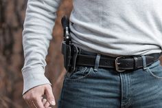 a man in jeans and a white shirt holding a black belted holster on his hip