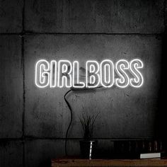 a neon sign that says girlboss on the wall next to a table with a potted plant