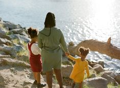 three children holding hands while standing on rocks near the water with their mother and father