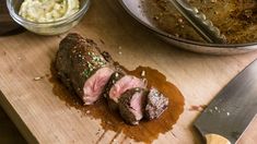 a piece of meat on a cutting board next to a bowl of mashed potatoes